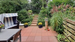 A garden patio with a table and chairs, a striped bench, and a wooden fence.