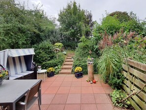 A garden patio with a table and chairs, a striped bench, and a wooden fence. - Urlauberdorf 29b, Deutschland (Ostseebad Boltenhagen)