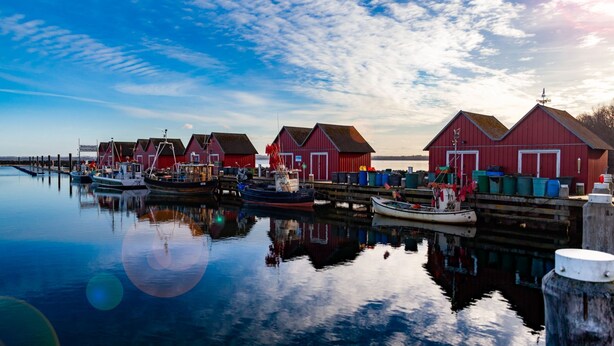 A waterfront scene with red buildings, boats, and calm water reflecting the structures.