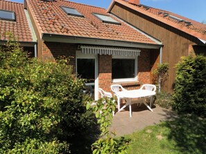 Una casa con techo de tejas, fachada de ladrillo y un patio con muebles blancos.
