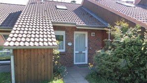 Ein zweistöckiges Haus mit Ziegeldach, Holzzaun und einem kleinen Garten mit Blumen und Sträuchern.