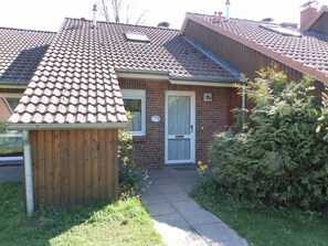 A two-story house with a tiled roof, a wooden fence, and a small garden with flowers and shrubs.