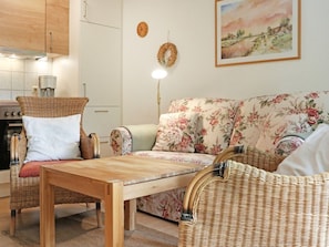 Un salon chaleureux avec une table basse en bois, des fauteuils en osier, un canapé à motifs floraux, une machine à café et un tableau accroché au mur.