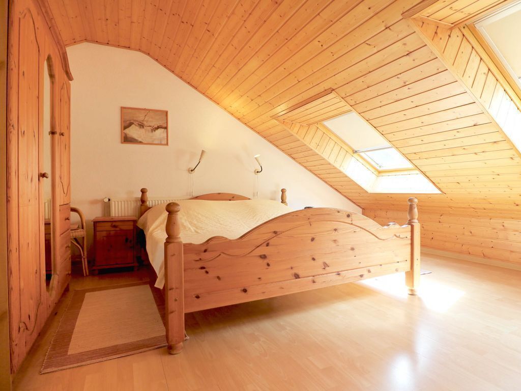 A bedroom with a wooden sloped ceiling, a bed, a nightstand, a radiator, and a skylight.