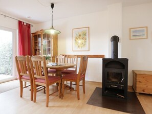 A dining area with wooden chairs and a table, a black wood-burning stove, and a wooden cabinet with glass doors.