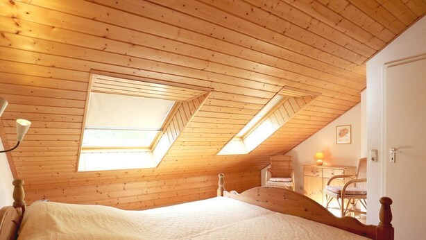Ein Schlafzimmer mit Holzbalkendecke, einem Bett und einem Schreibtisch mit Stuhl.