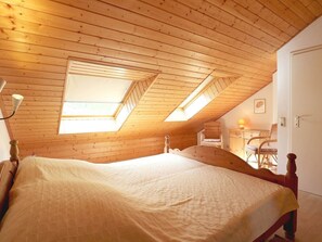 A bedroom with a wooden ceiling, a bed, and a desk with a chair.
