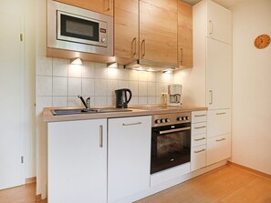 Una cocina compacta con gabinetes blancos, un microondas integrado, una estufa y una cafetera.