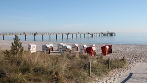 Ein Strand mit einem Steg, der sich in ruhiges Wasser erstreckt, Strandkörben und einem Sandweg.