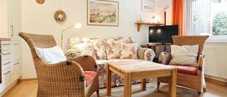 Un salon avec des meubles en osier, un canapé, une table basse, un téléviseur à écran plat et une fenêtre avec des rideaux.