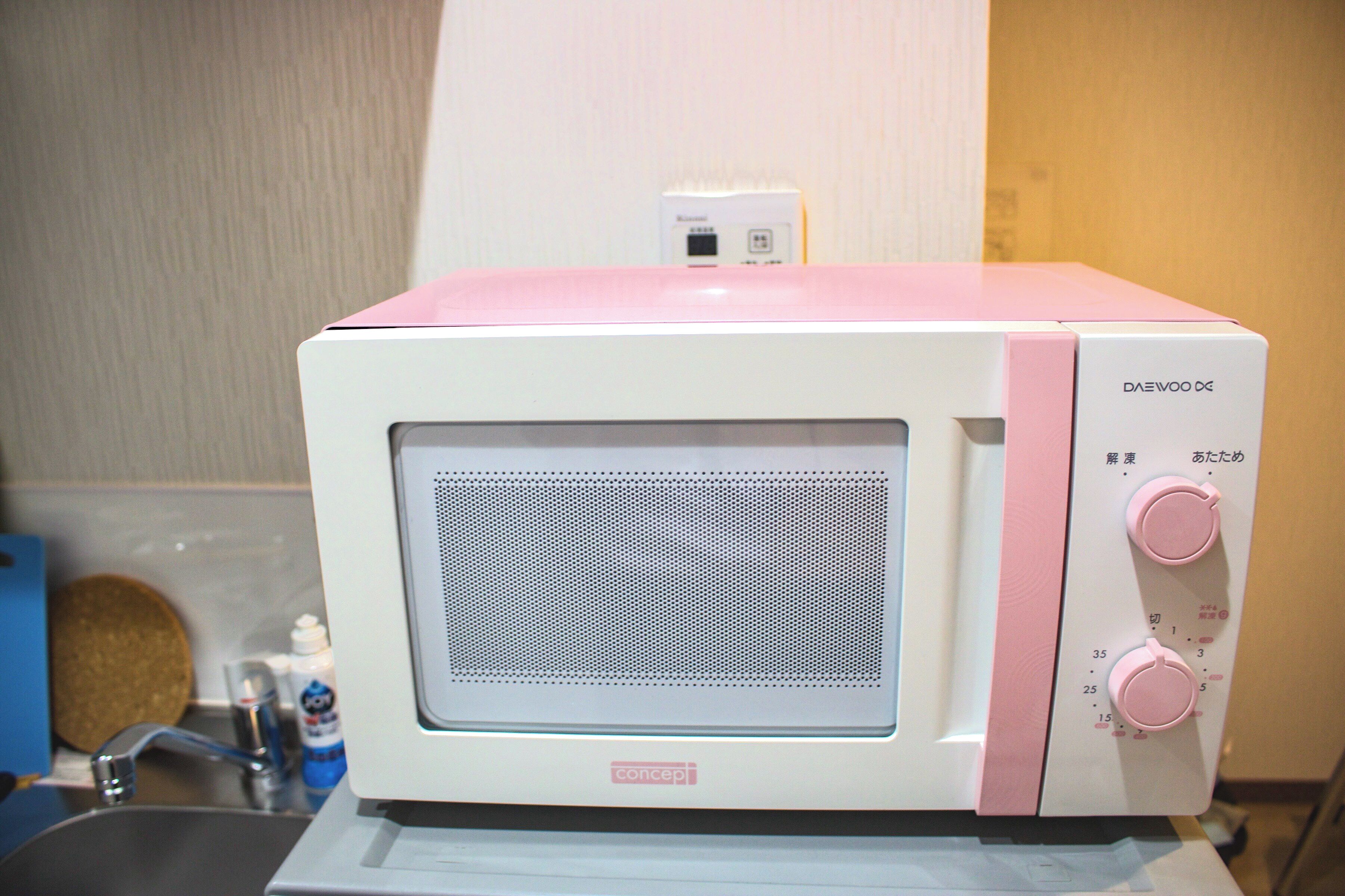 Un four à micro-ondes aux couleurs rose et blanc, doté d’un écran numérique et d’un panneau de commande avec des boutons.