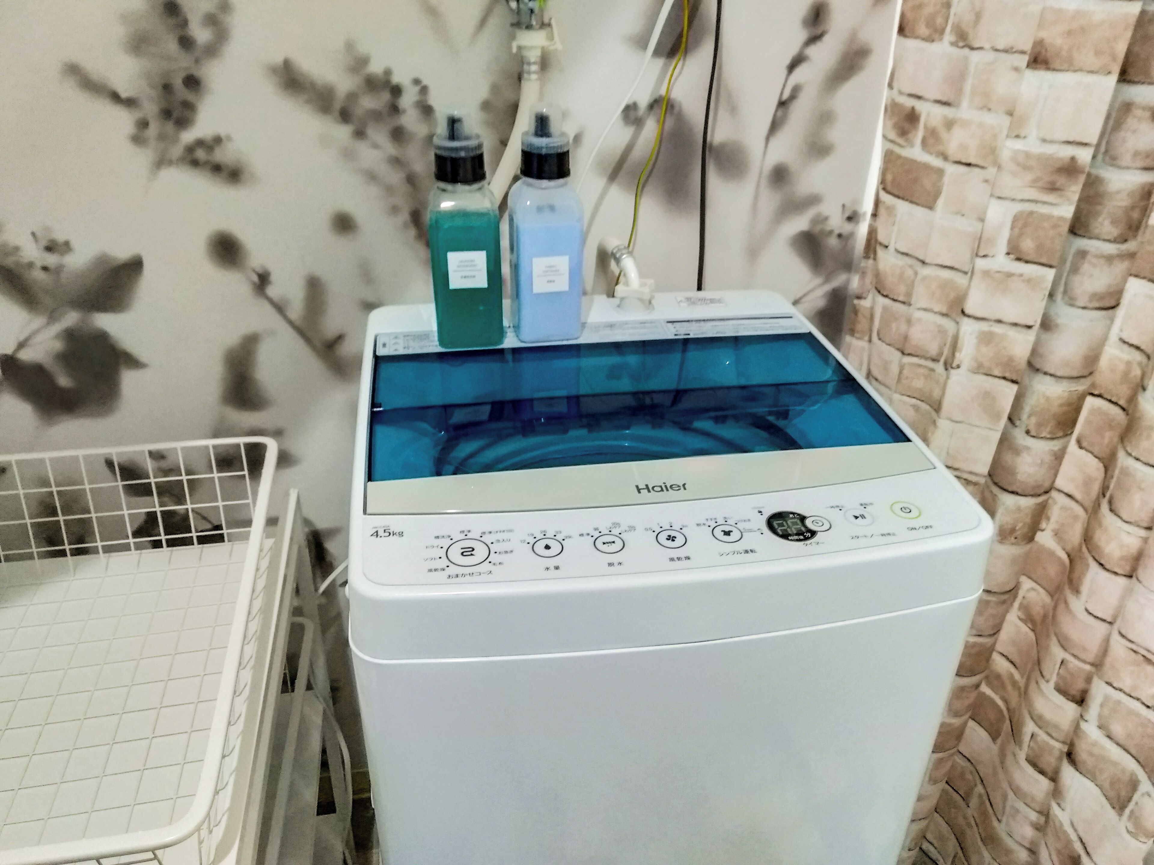 A front-loading Haier washing machine with a 4.5kg capacity, placed in a laundry area with a tiled floor and a brick-patterned wall.
