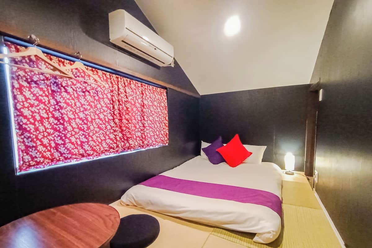 A modern hotel room with a bed, a small table, and a window with a floral curtain.