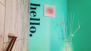 A staircase with a handrail, a teal wall, a framed floral artwork, and a decorative vase with branches and spherical ornaments. - Sakura Villa Osaka (Osaka)