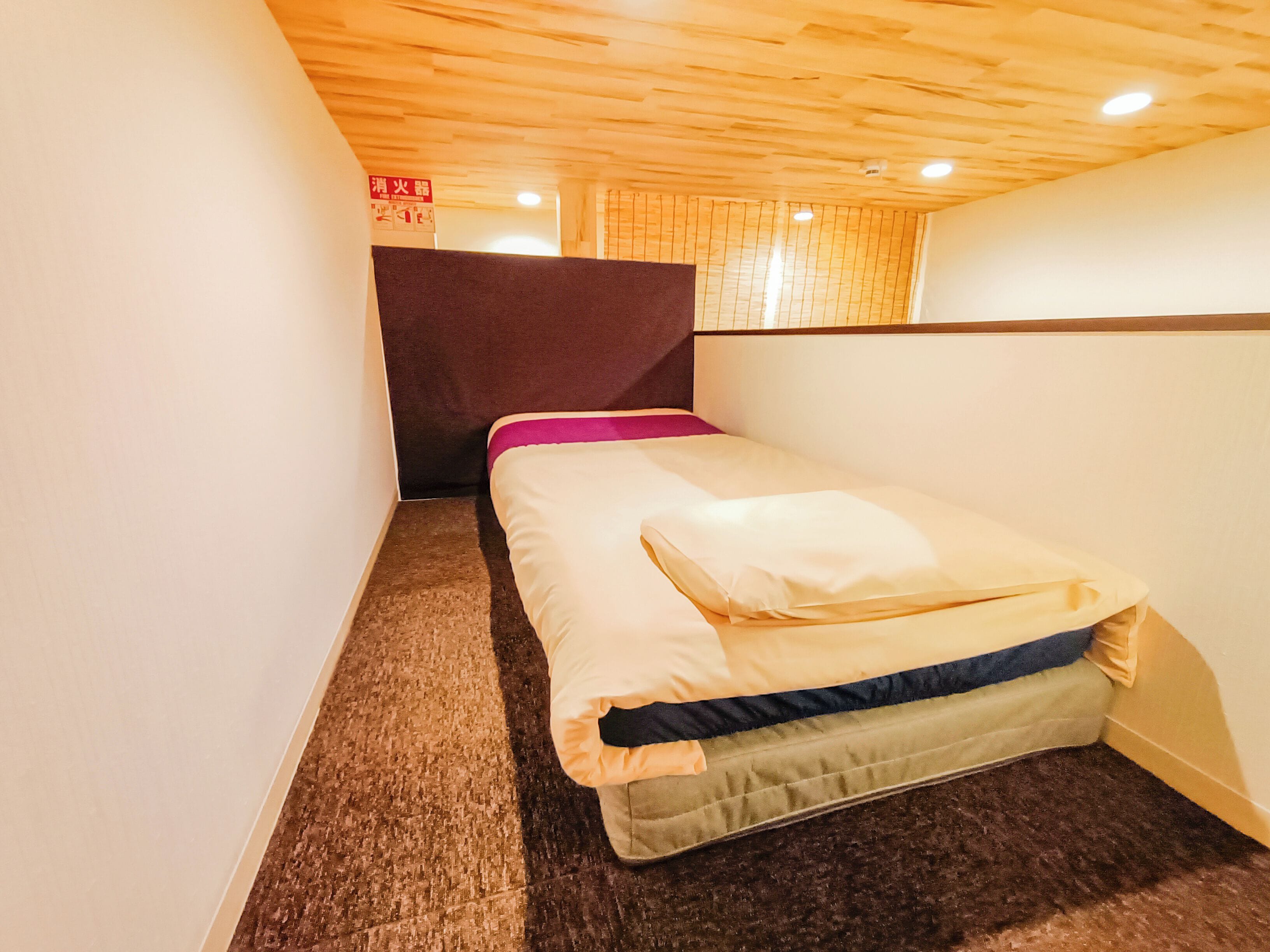 A small, cozy room with a single bed, a wooden ceiling, and a carpeted floor.