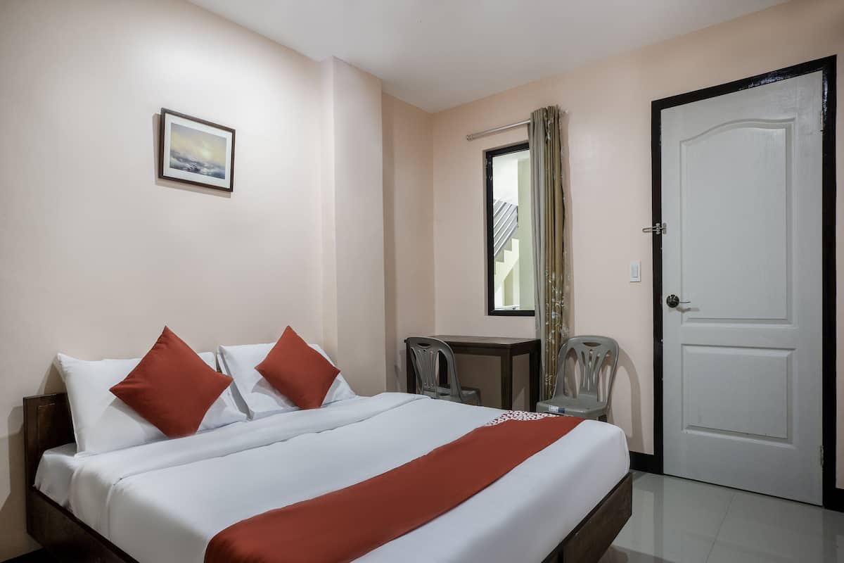 A hotel room with a bed, a desk, a chair, a window with curtains, and a door.