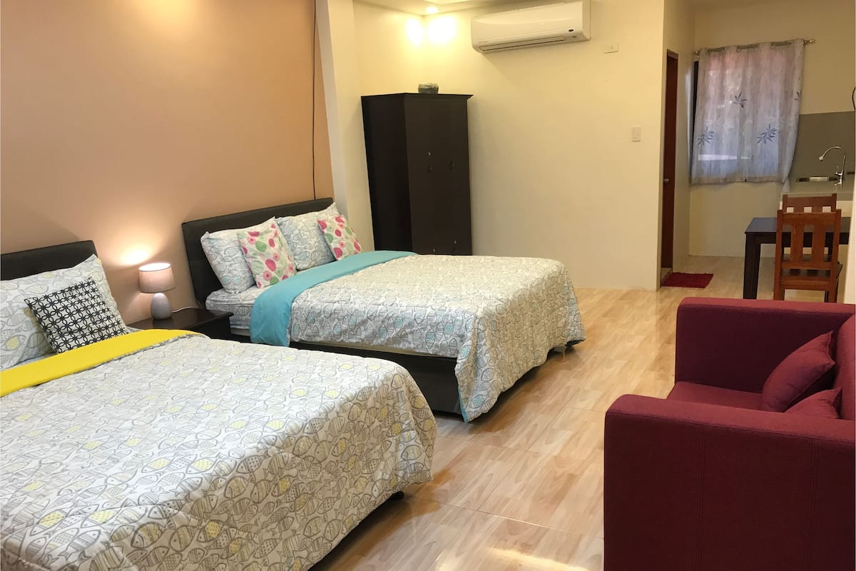 Una habitación de hotel con dos camas, una silla roja, un escritorio y un equipo de aire acondicionado.