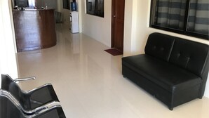 A hotel lobby with a black leather sofa, a reception desk, a water cooler, and a TV screen.