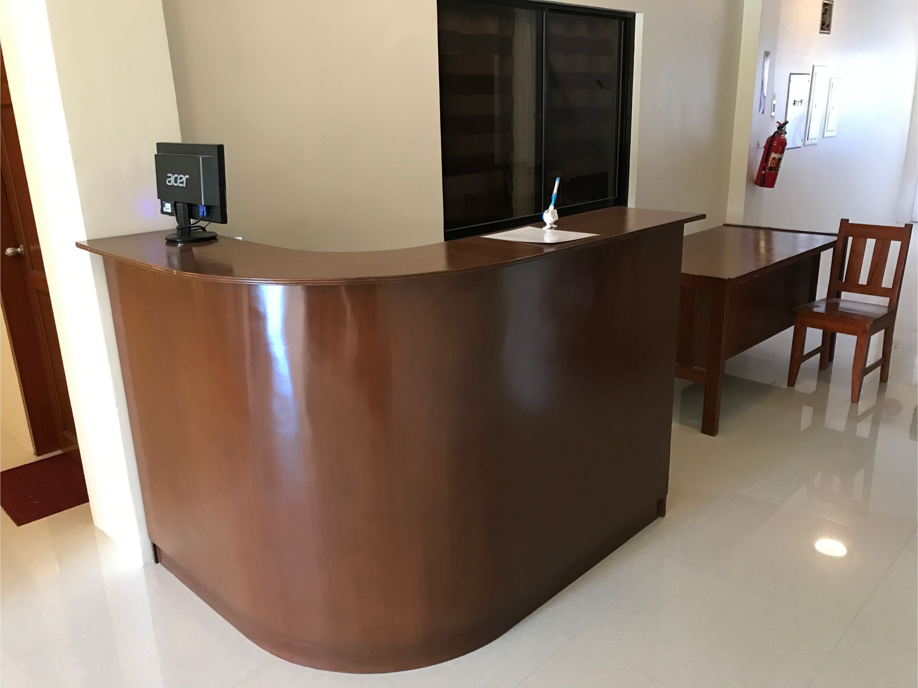 A reception desk with a flat-screen monitor, a fire extinguisher, and a wooden chair.