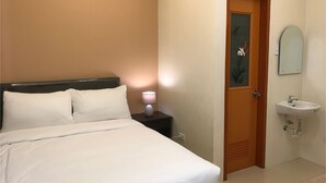 A hotel room with a bed, a nightstand with a lamp, a door, and a bathroom with a sink and mirror.