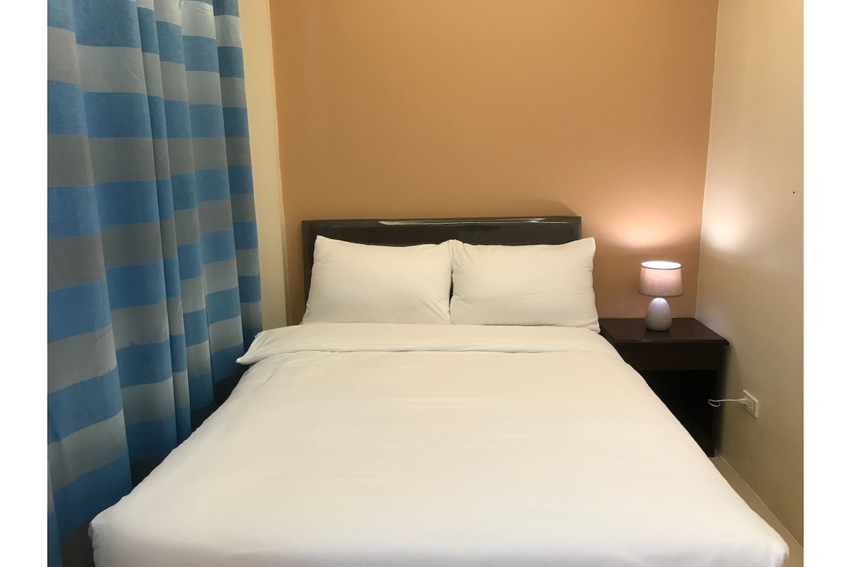 A hotel room with a bed, a nightstand with a lamp, and a blue-striped curtain.