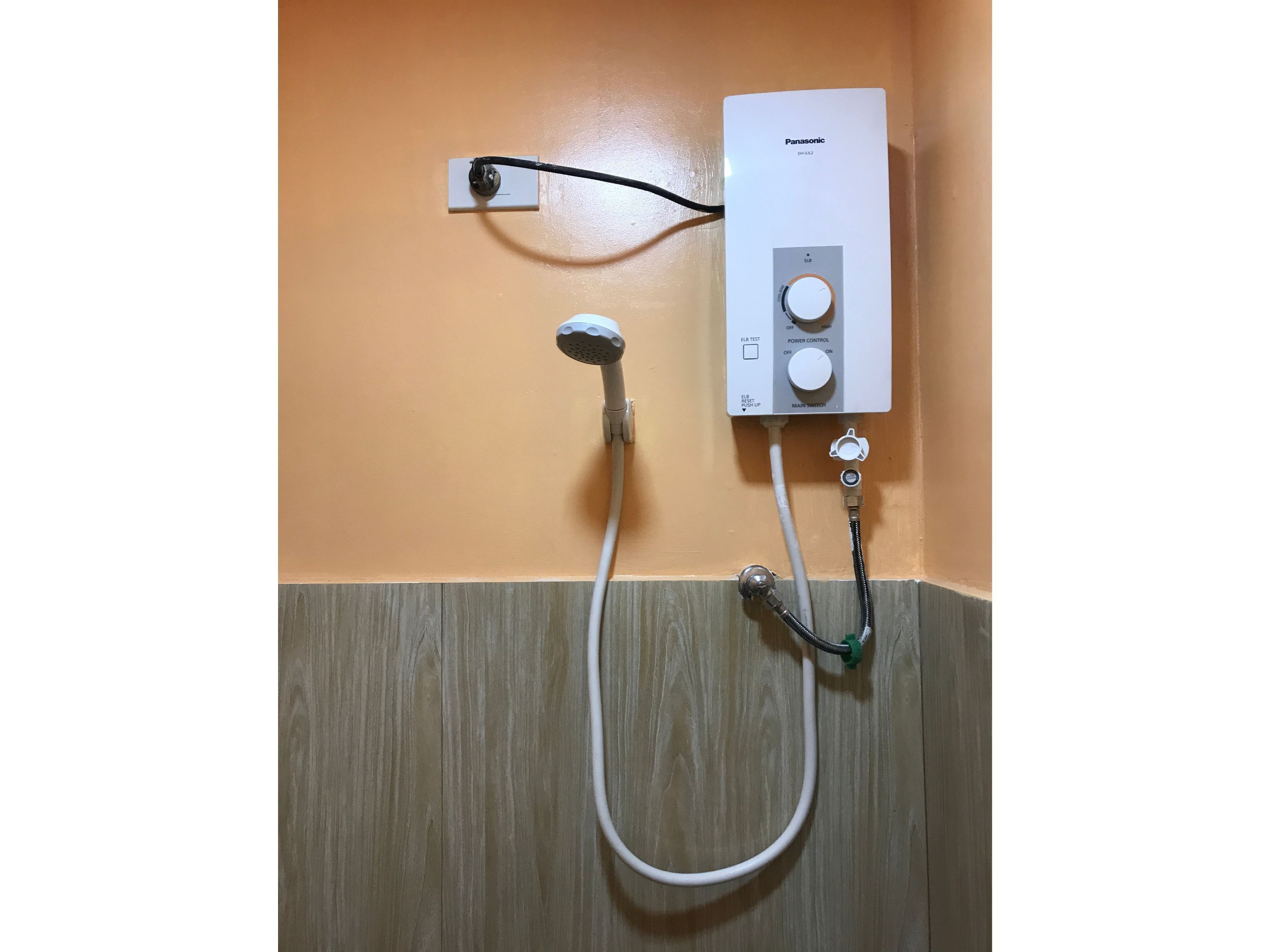 A bathroom with a white Panasonic water heater mounted on an orange wall, connected to a showerhead.