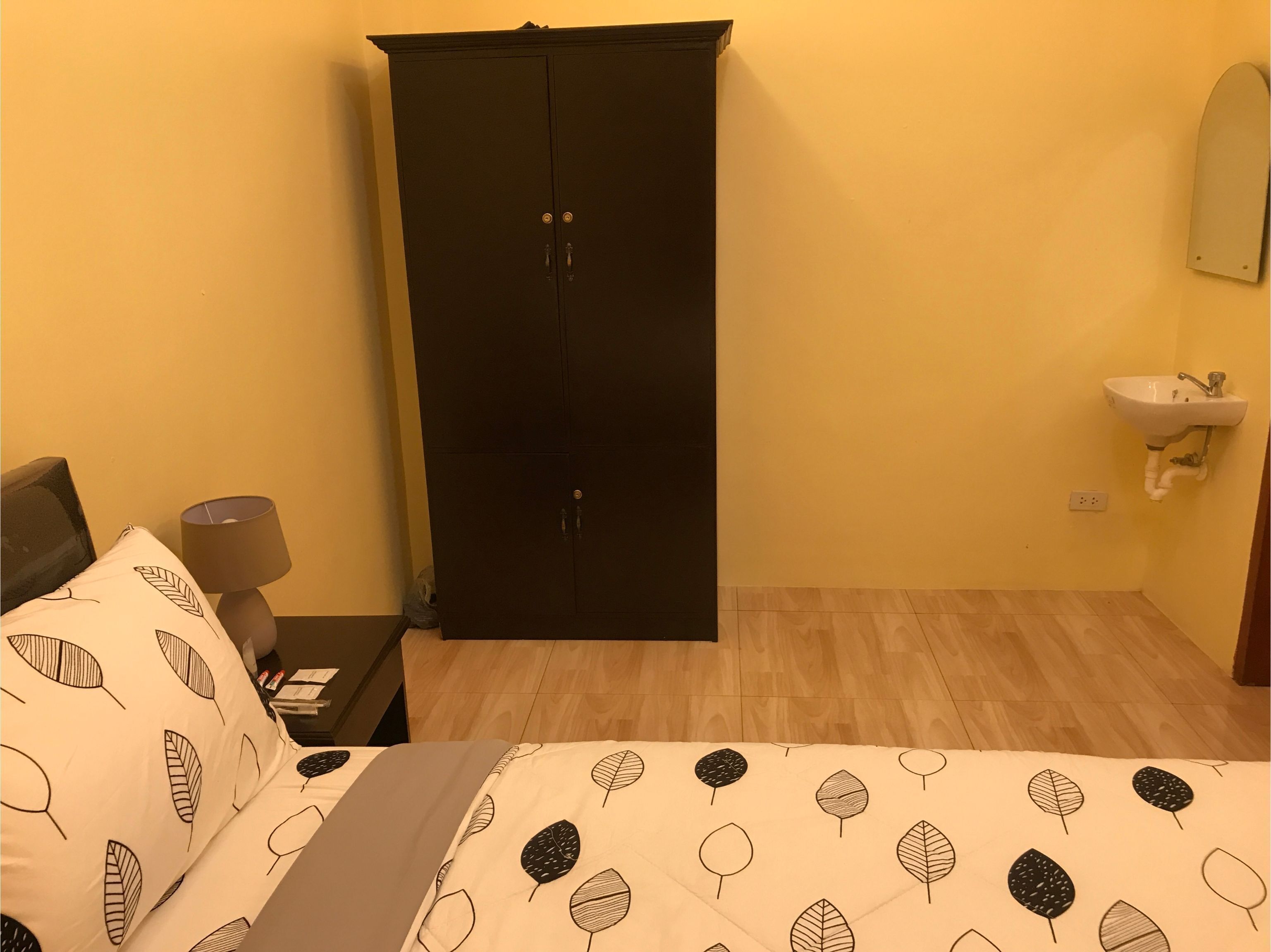 A bedroom with a bed, a wardrobe, a bedside table with a lamp, and a wall-mounted sink.