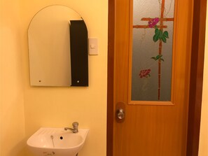 A bathroom with a white sink, a mirror, and a door with a frosted glass panel featuring a floral design. - Guest Hotel (Pili)