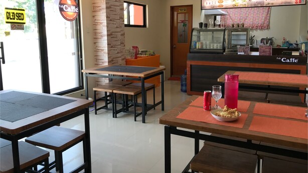 A cafe interior with tables, chairs, a menu board, and a kitchen area.