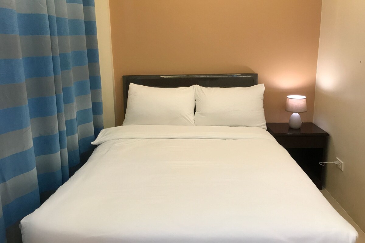 Una habitación de hotel con una cama, una mesita de noche con lámpara y una cortina azul a rayas.