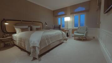 A hotel room with a large bed, two chairs, a nightstand, and a window with a view.