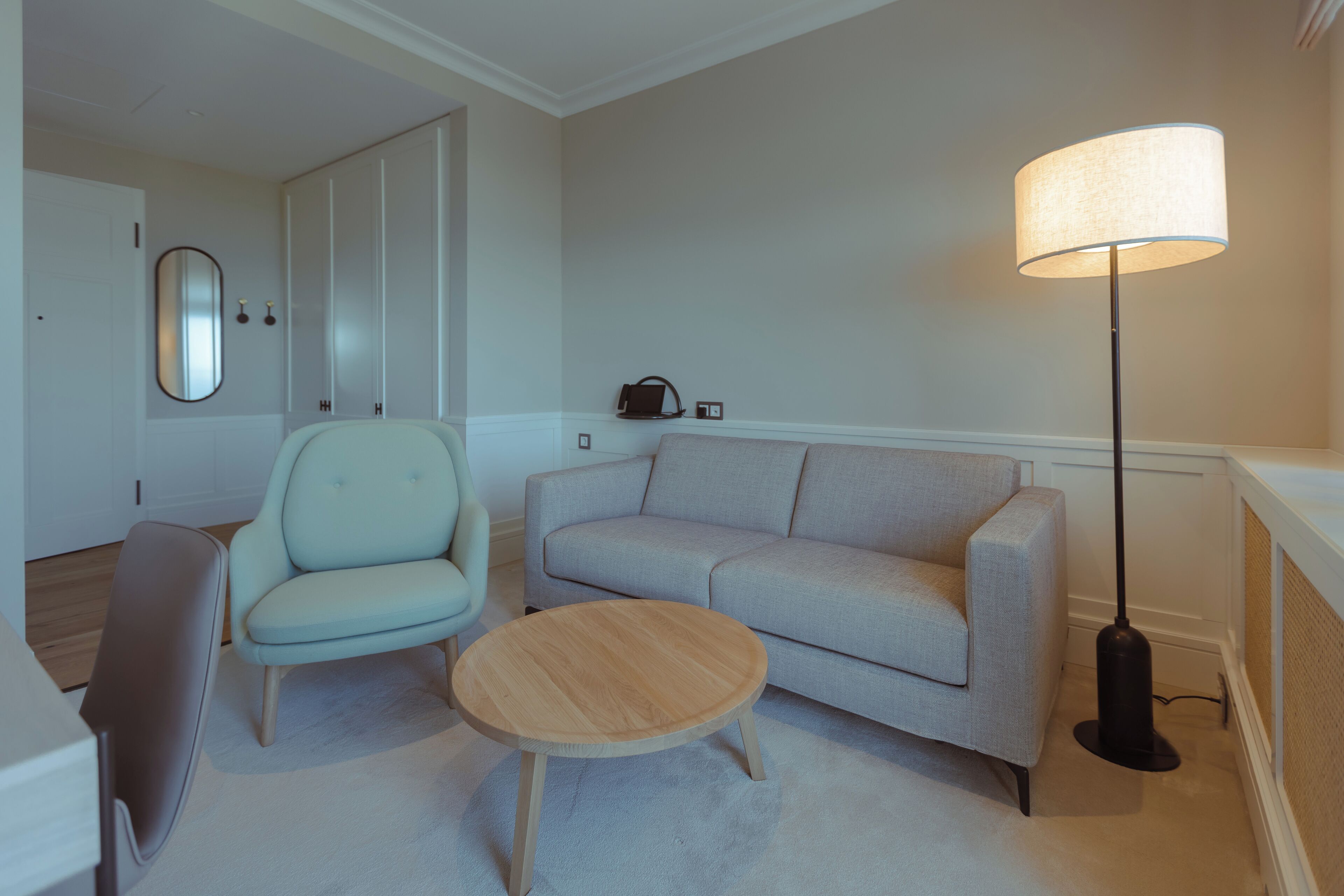 A modern living room with a sofa, armchair, coffee table, floor lamp, and a mirror on the wall.