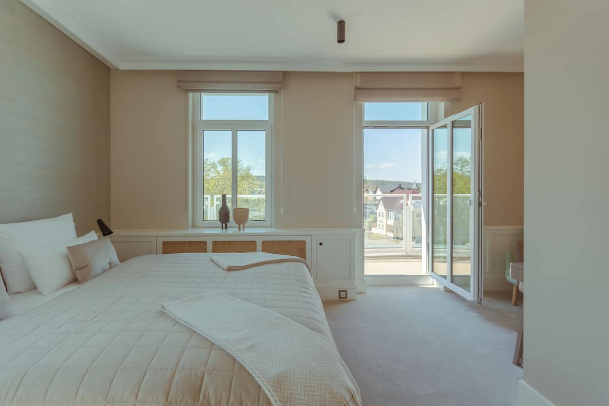 Ein Schlafzimmer mit einem großen Bett, zwei Fenstern, einer Heizung und Blick nach draußen.