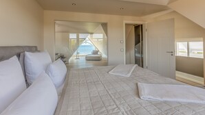 A bedroom with a large bed, a sofa, and a view of the sea through a glass door. - Strandhotel Ostende (Heringsdorf)