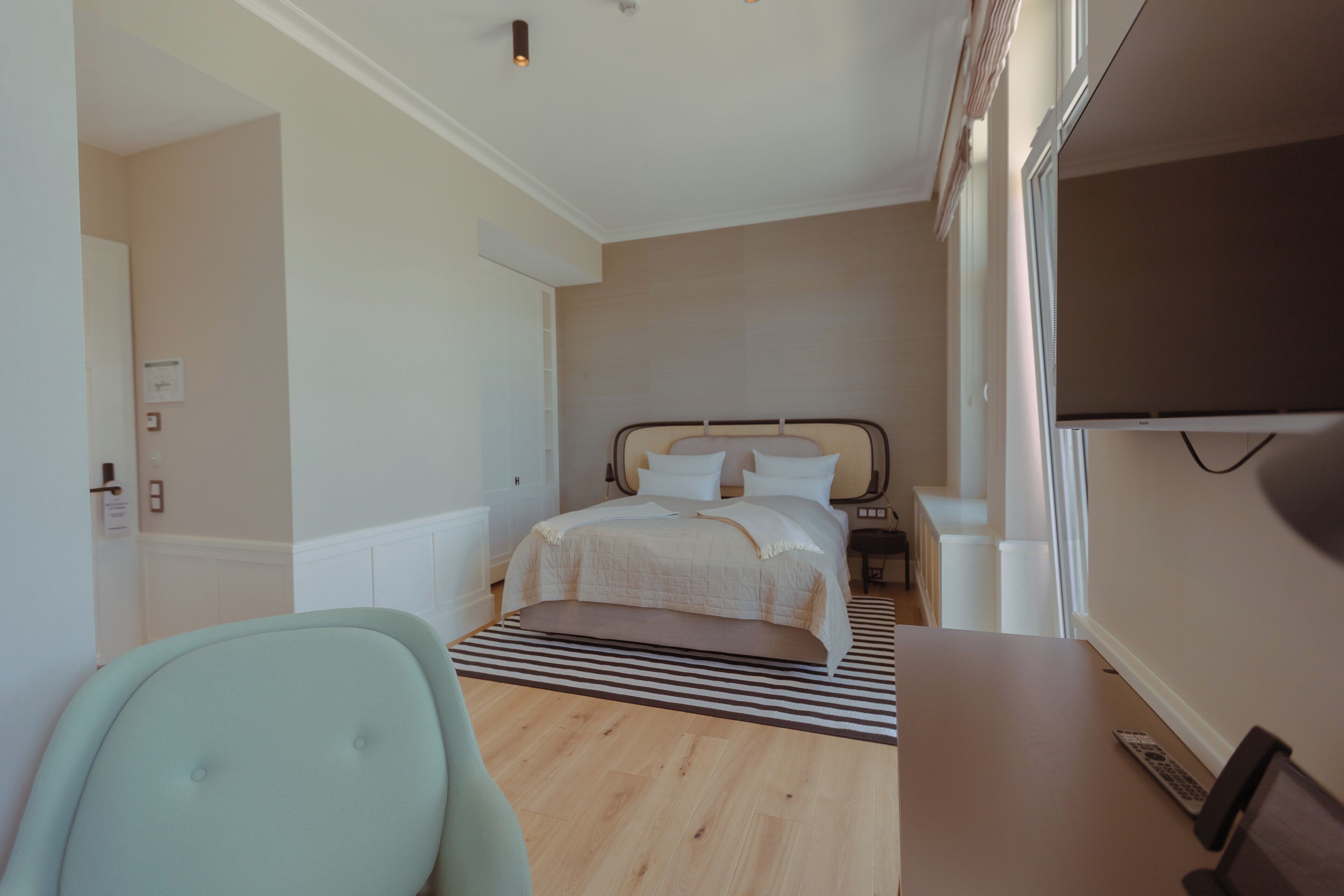 A modern hotel room with a bed, a desk, a chair, and a TV.