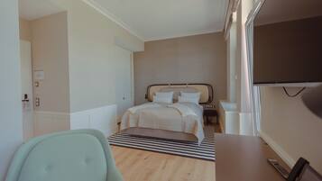 A modern hotel room with a bed, a desk, a chair, and a TV.