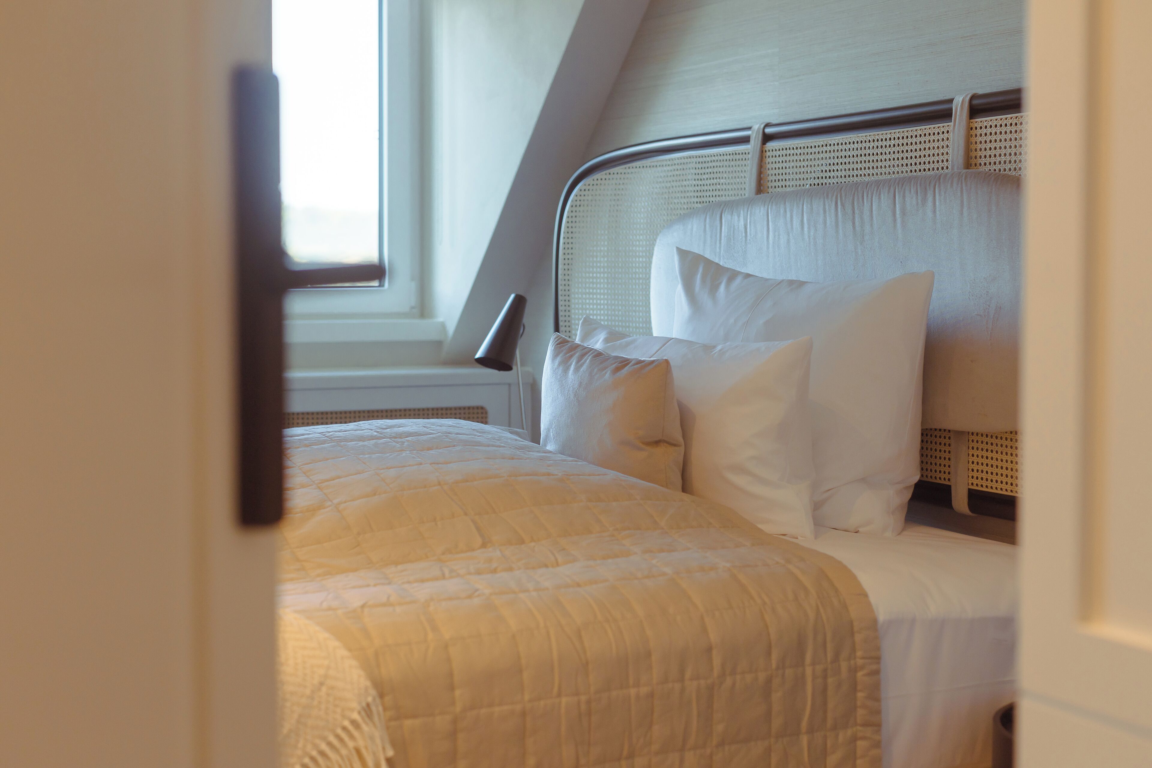 A neatly made bed with a white comforter and pillows, a metal headboard, and a window with blinds.