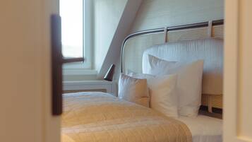 A neatly made bed with a white comforter and pillows, a metal headboard, and a window with blinds.