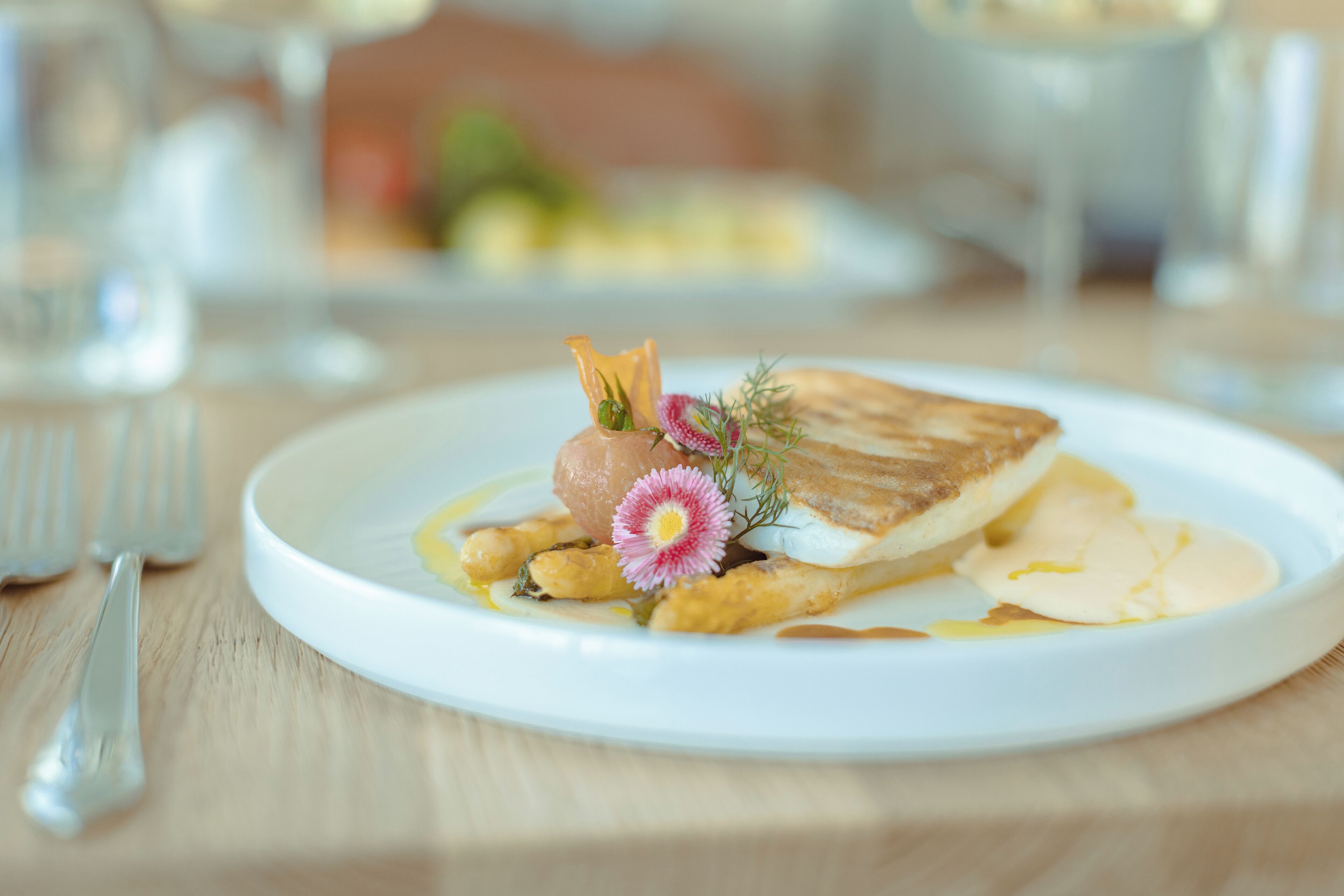 Um prato branco com um prato de peixe, decorado com endro e uma flor rosa, sobre uma mesa de madeira.