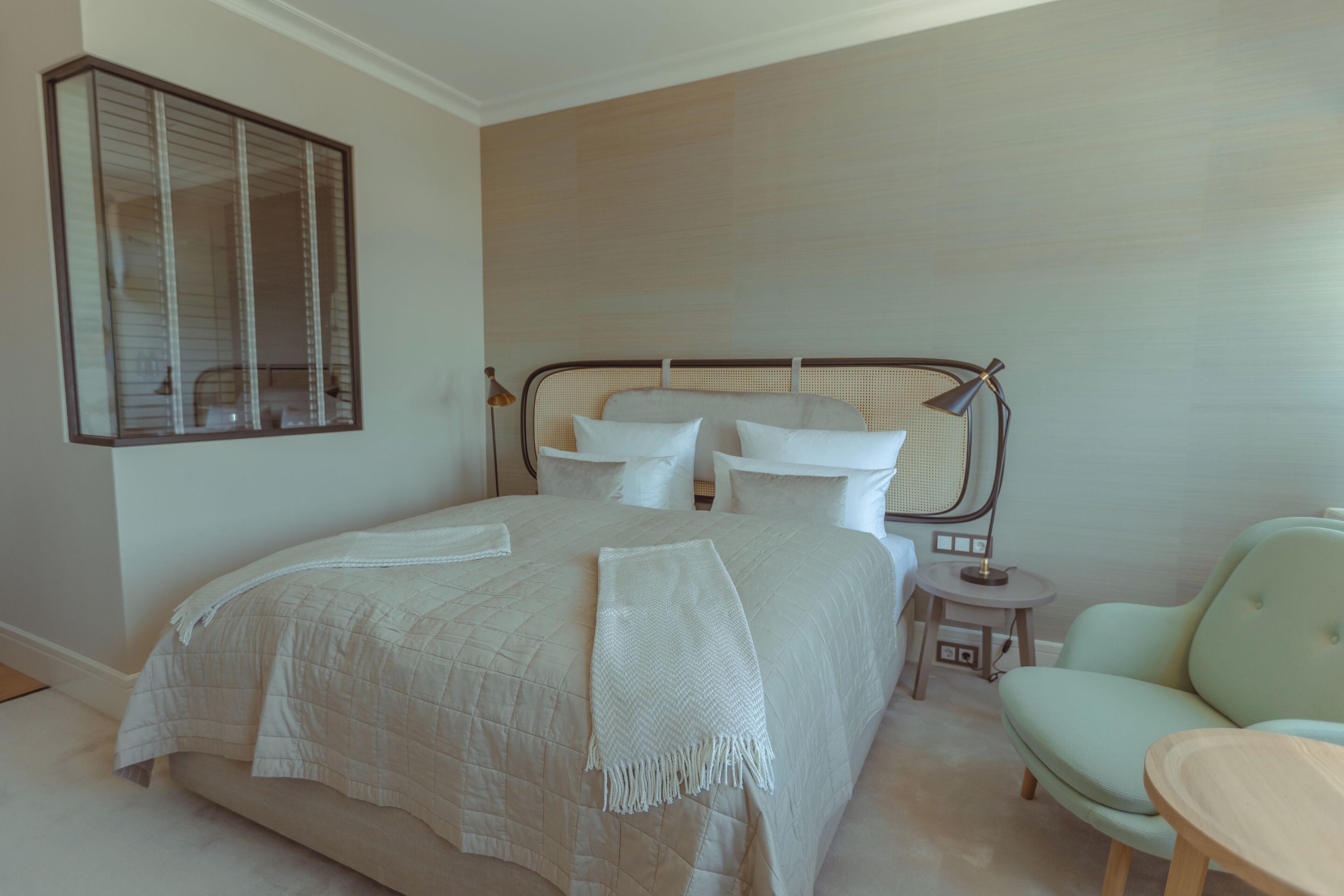 Un dormitorio ordenado con una cama grande, una mesita de noche, una silla y un espejo en la pared.