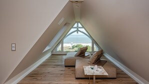 A modern loft bedroom with a sloped ceiling, a large window overlooking the beach, a cozy sofa, and a small table. - Strandhotel Ostende (Heringsdorf)