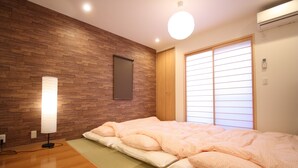 A bedroom with a wooden wall, a bed with pink bedding, a standing lamp, and a window with blinds. - GuestHouse SagaArashiyama (Kyoto)