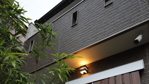 A modern building with a wooden sliding door and a small illuminated sign above it. - GuestHouse SagaArashiyama (Kyoto)