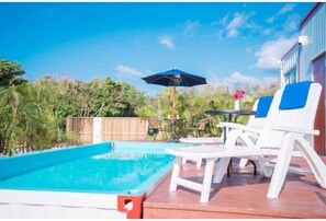 Relax by the pool surrounded by lush greenery and shaded by a blue umbrella.