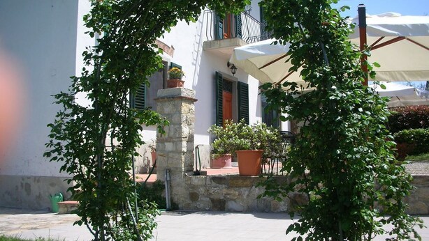 Une cour avec une fontaine en pierre, des plantes en pot et un bâtiment blanc aux volets verts.