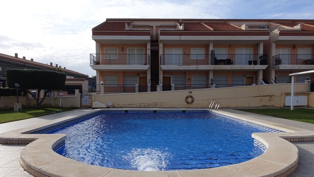 A swimming pool with a tiled border, surrounded by a building with balconies and a lifebuoy on the wall.