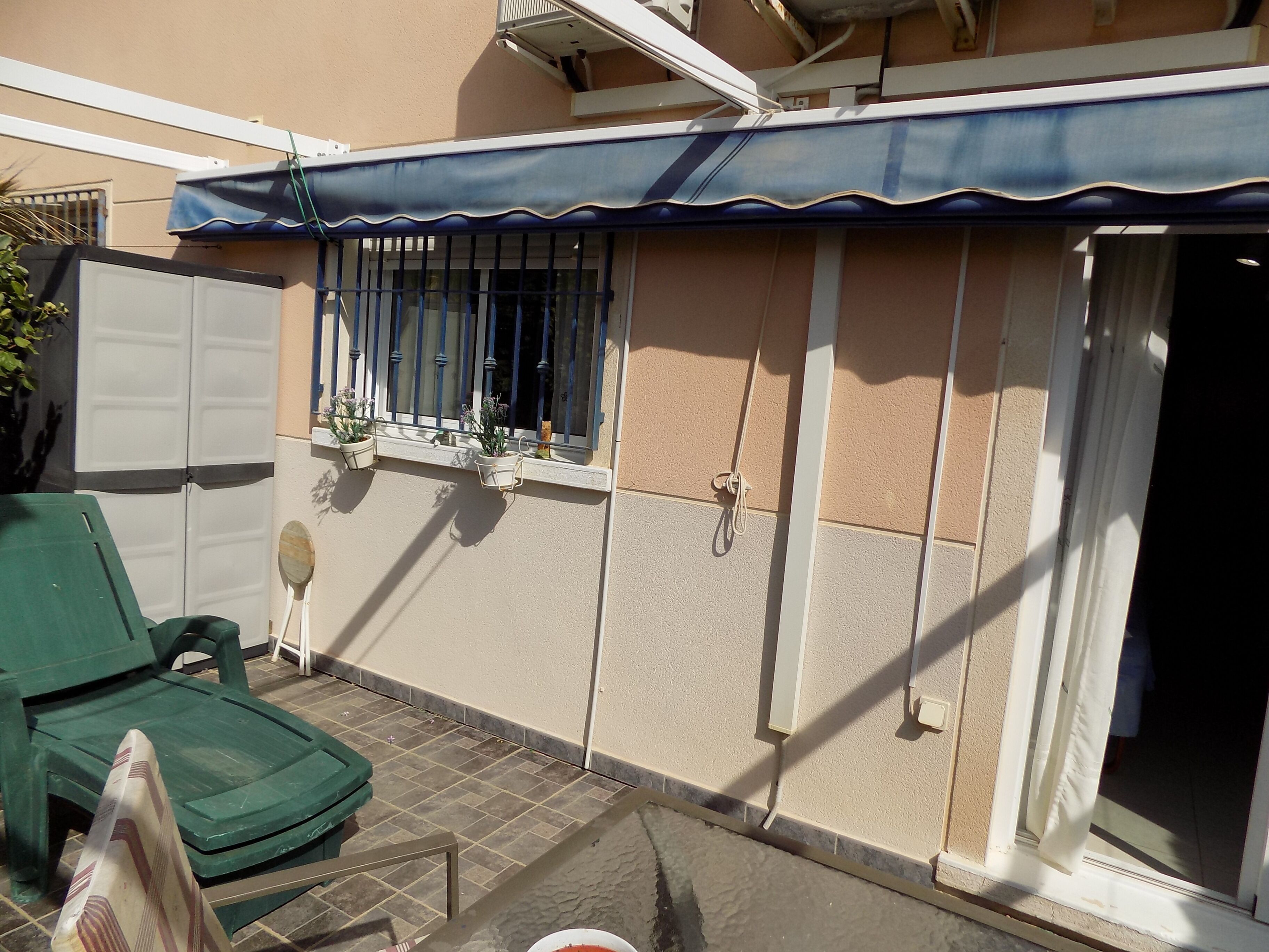 A small outdoor area with a green chair, a window with metal bars, and a white door.