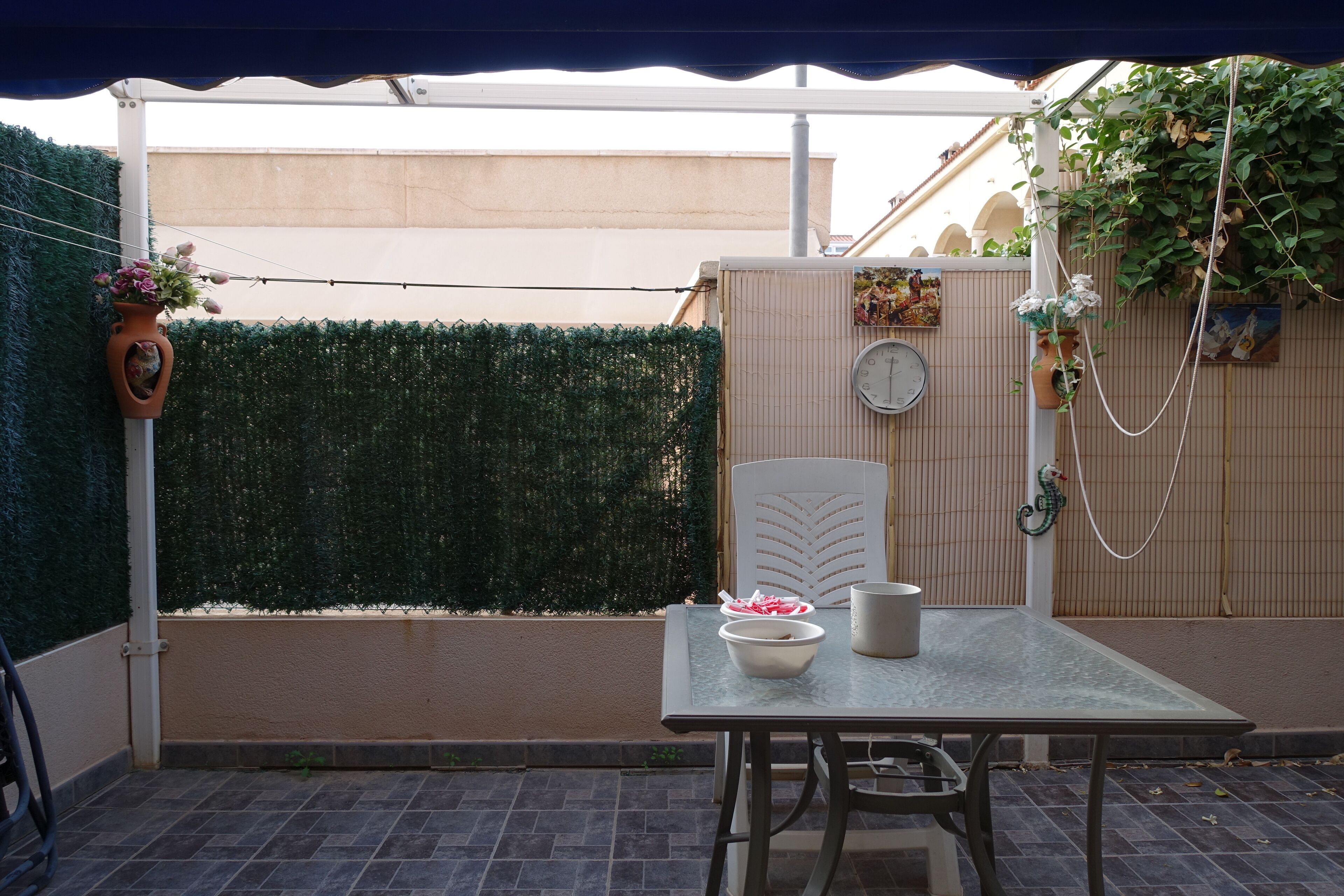 Un patio con una mesa, sillas, una planta en maceta y un reloj en la pared.