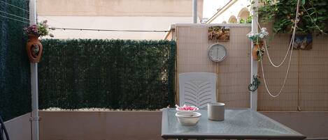Un patio con una mesa, sillas, una planta en maceta y un reloj en la pared.