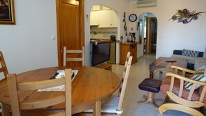 A dining area with a wooden table and chairs, a television, and a kitchen in the background.
